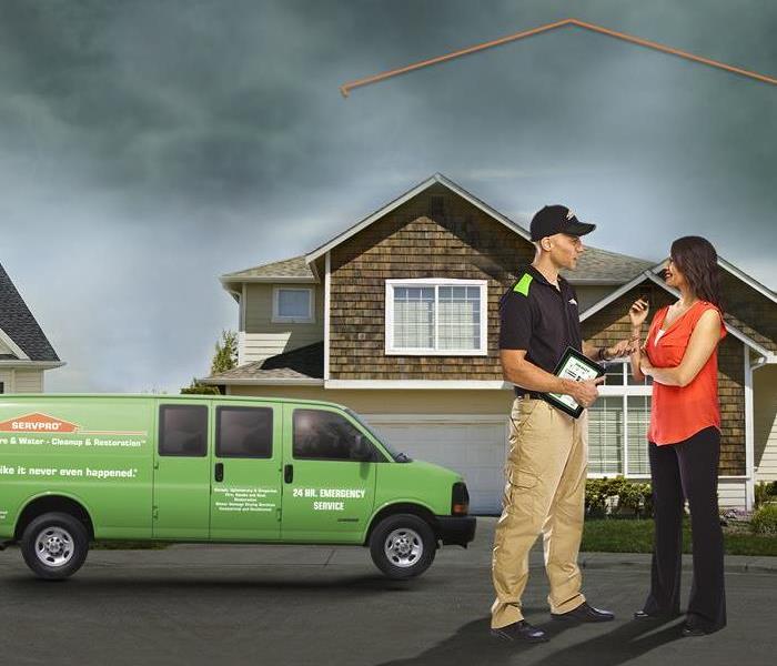 A SERVPRO member and a woman in front of a house with a storm in the background